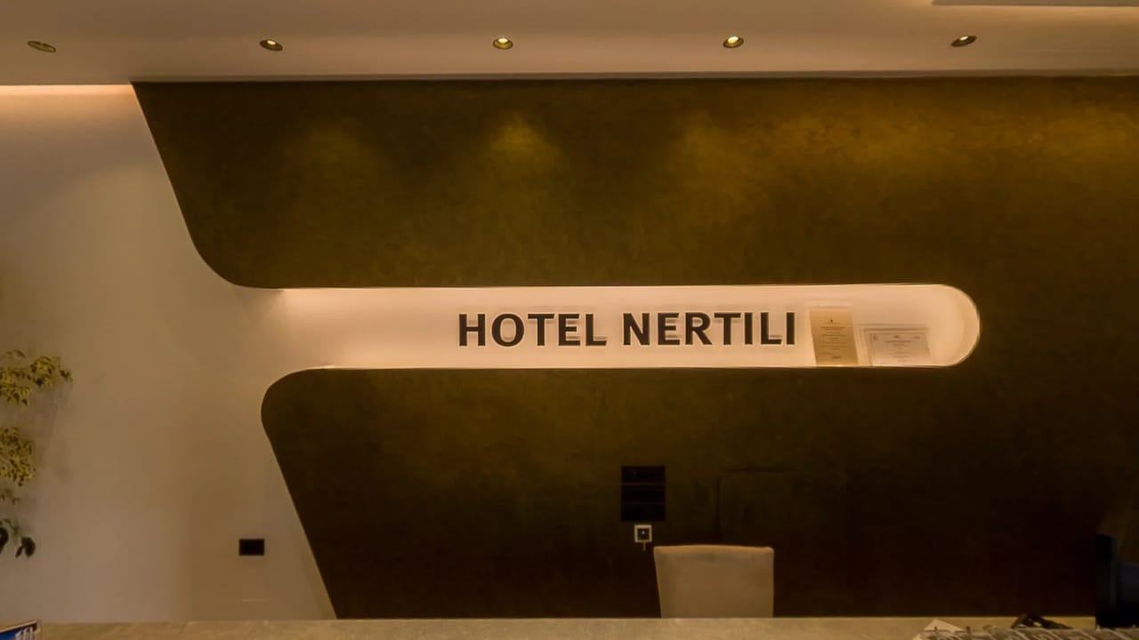 The reception desk at Hotel Nertili under a lit sign carrying the hotel's name